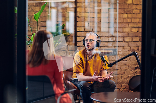 Image of A gathering of young business professionals, some seated in a glass-walled office, engage in a lively conversation and record an online podcast, embodying modern collaboration and dynamic interaction