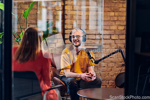 Image of A gathering of young business professionals, some seated in a glass-walled office, engage in a lively conversation and record an online podcast, embodying modern collaboration and dynamic interaction