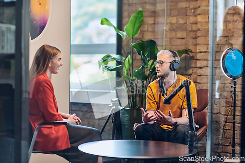 Image of A gathering of young business professionals, some seated in a glass-walled office, engage in a lively conversation and record an online podcast, embodying modern collaboration and dynamic interaction