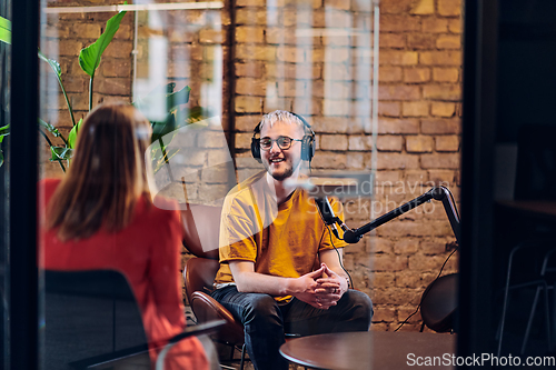 Image of A gathering of young business professionals, some seated in a glass-walled office, engage in a lively conversation and record an online podcast, embodying modern collaboration and dynamic interaction