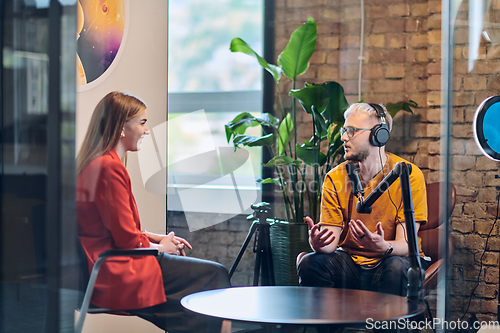 Image of A gathering of young business professionals, some seated in a glass-walled office, engage in a lively conversation and record an online podcast, embodying modern collaboration and dynamic interaction