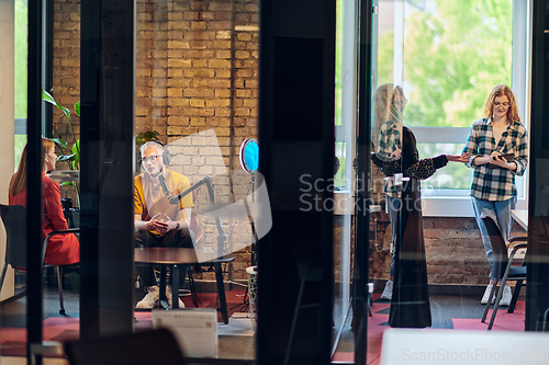 Image of A gathering of young business professionals, some seated in a glass-walled office, engage in a lively conversation and record an online podcast, embodying modern collaboration and dynamic interaction