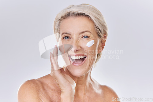 Image of Beauty, skincare and wellness with a senior woman applying lotion, sunscreen or serum to her face in studio on a grey background. Health, skin care and motivation with a beautiful and healthy model