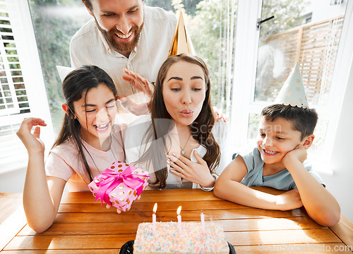Image of Birthday, family and celebration with a woman blowing the candles on her cake. Husband and kids spoiling mom and making her feel happy on her special day mothers day while having a party at home