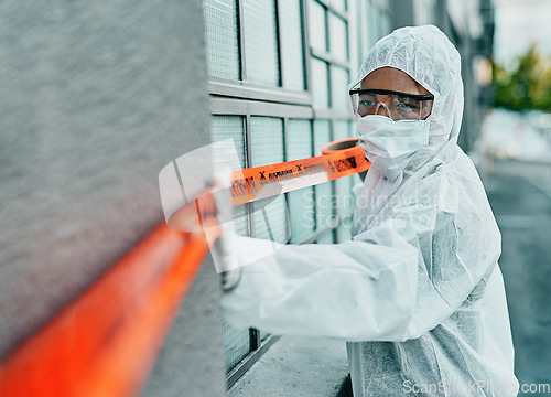 Image of Covid healthcare worker responding to a biohazard in a public area using barrier tape outside. First responder in protection hazmat suit and mask separating a space due to a new pandemic or outbreak