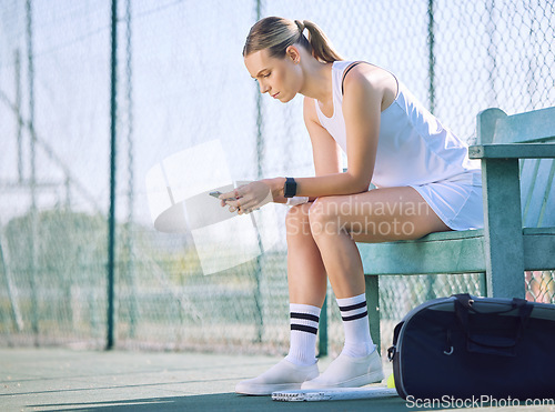 Image of Female tennis player with a phone checking fitness goal progress on modern exercise app online while taking a break on the court. A sports woman looking at messages on cellphone and waiting for coach