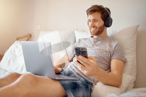 Image of 5g internet, video and online streaming of a man on a computer and phone in bed. Happy guy with a smile relax and multitask listening to a digital radio podcast or web music with modern technology