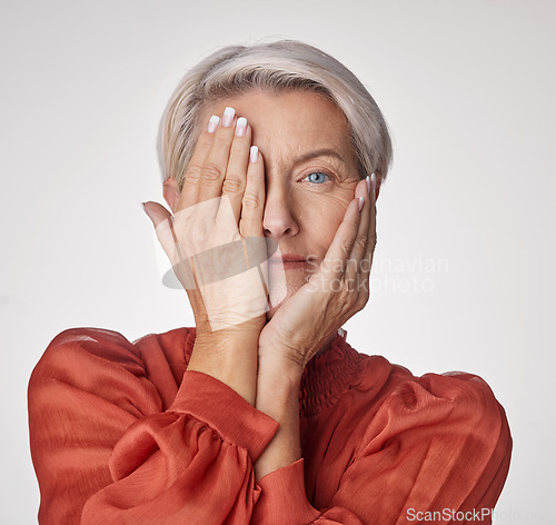 Image of Beauty, health and wellness with a senior woman touching her face with her hands on a studio background. Headshot portrait of a person covering her eye with her hand to show good vision and skincare