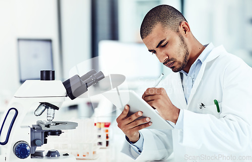 Image of Serious male scientist working on a tablet reviewing an online phd publication in a lab. Laboratory worker updating health data for a science journal. Medical professional document clinical trial