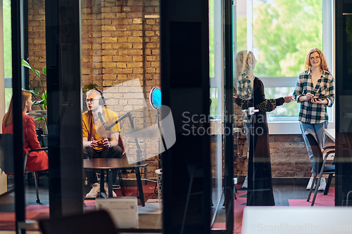 Image of A gathering of young business professionals, some seated in a glass-walled office, engage in a lively conversation and record an online podcast, embodying modern collaboration and dynamic interaction