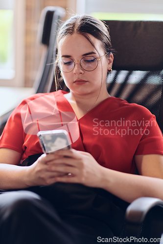 Image of A businesswoman resting on a short break from work in a modern startup coworking center, using her smartphone to unwind and recharge.