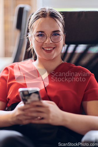 Image of A businesswoman resting on a short break from work in a modern startup coworking center, using her smartphone to unwind and recharge.