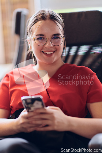 Image of A businesswoman resting on a short break from work in a modern startup coworking center, using her smartphone to unwind and recharge.