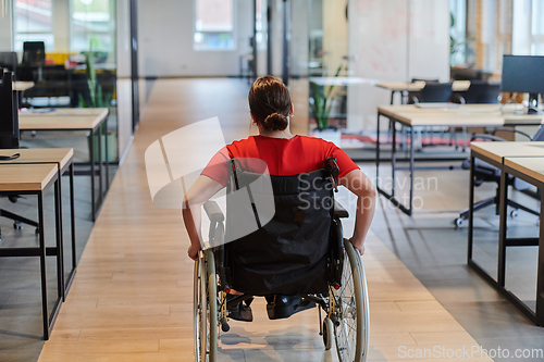 Image of A modern young businesswoman in a wheelchair is surrounded by an inclusive workspace with glass-walled offices, embodying determination and innovation in the business world