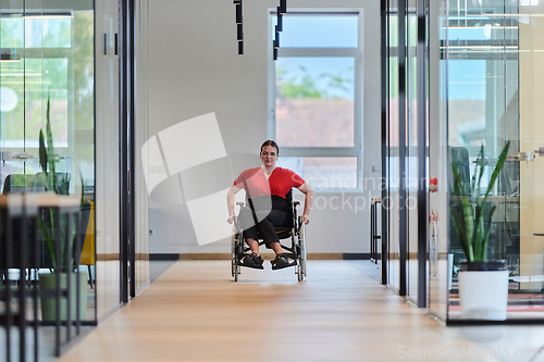 Image of A modern young businesswoman in a wheelchair is surrounded by an inclusive workspace with glass-walled offices, embodying determination and innovation in the business world