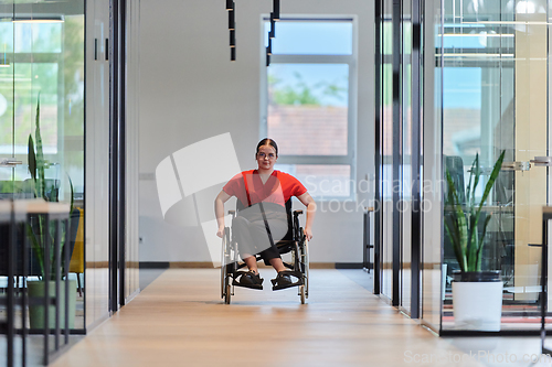 Image of A modern young businesswoman in a wheelchair is surrounded by an inclusive workspace with glass-walled offices, embodying determination and innovation in the business world