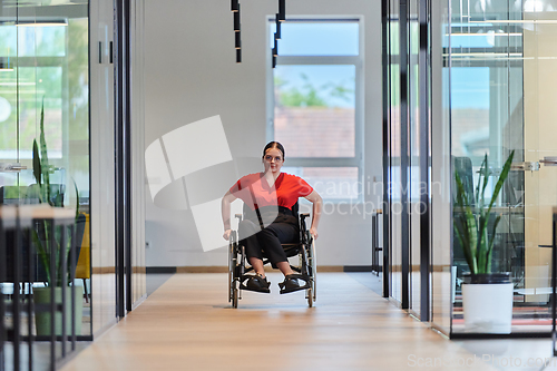 Image of A modern young businesswoman in a wheelchair is surrounded by an inclusive workspace with glass-walled offices, embodying determination and innovation in the business world