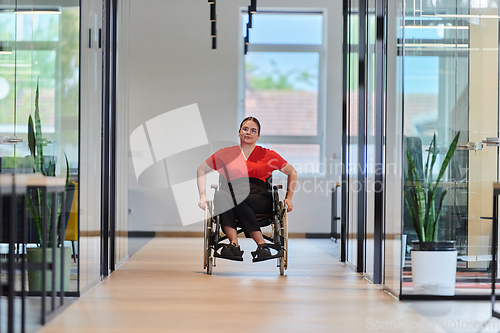 Image of A modern young businesswoman in a wheelchair is surrounded by an inclusive workspace with glass-walled offices, embodying determination and innovation in the business world