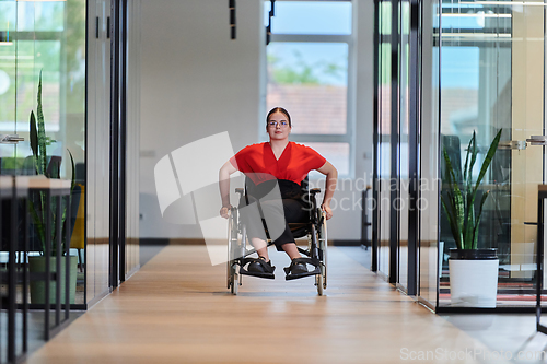 Image of A modern young businesswoman in a wheelchair is surrounded by an inclusive workspace with glass-walled offices, embodying determination and innovation in the business world