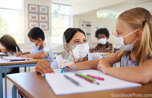 Image of Covid, education and learning with a teacher helping a student during class at school with classmates in the background. Female educator wearing a mask and assisting a girl child with her study work