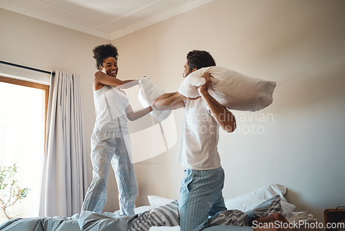 Image of Pillow fight, playing and bonding with a happy couple playing, bonding and spending time together in their bedroom at home. Laughing, having fun and feeling carefree in pyjamas over the weekend