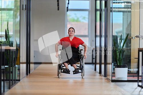 Image of A modern young businesswoman in a wheelchair is surrounded by an inclusive workspace with glass-walled offices, embodying determination and innovation in the business world