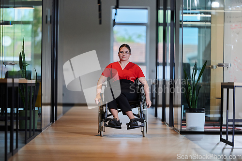 Image of A modern young businesswoman in a wheelchair is surrounded by an inclusive workspace with glass-walled offices, embodying determination and innovation in the business world