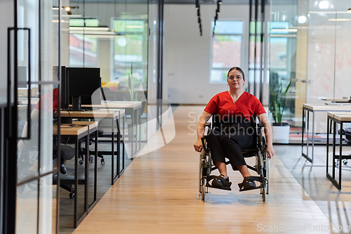 Image of A modern young businesswoman in a wheelchair is surrounded by an inclusive workspace with glass-walled offices, embodying determination and innovation in the business world