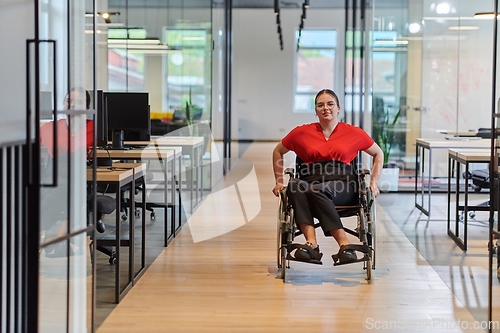 Image of A modern young businesswoman in a wheelchair is surrounded by an inclusive workspace with glass-walled offices, embodying determination and innovation in the business world