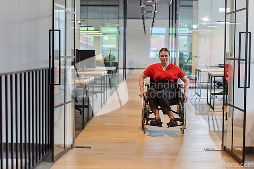 Image of A modern young businesswoman in a wheelchair is surrounded by an inclusive workspace with glass-walled offices, embodying determination and innovation in the business world