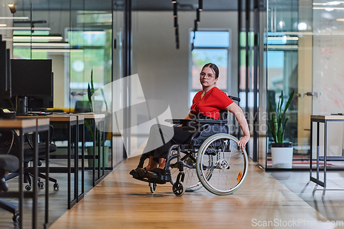 Image of A modern young businesswoman in a wheelchair is surrounded by an inclusive workspace with glass-walled offices, embodying determination and innovation in the business world