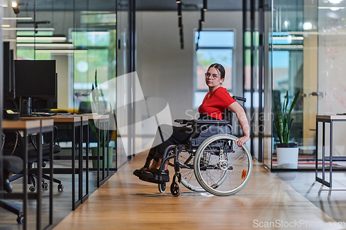 Image of A modern young businesswoman in a wheelchair is surrounded by an inclusive workspace with glass-walled offices, embodying determination and innovation in the business world