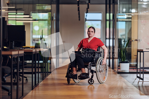 Image of A modern young businesswoman in a wheelchair is surrounded by an inclusive workspace with glass-walled offices, embodying determination and innovation in the business world