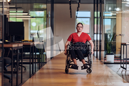 Image of A modern young businesswoman in a wheelchair is surrounded by an inclusive workspace with glass-walled offices, embodying determination and innovation in the business world