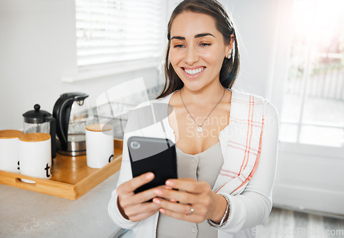 Image of Woman browsing, texting and reading on a phone in her kitchen at home. Smiling woman on social media online app, networking and messaging contacts while smiling at a funny post, meme or videos