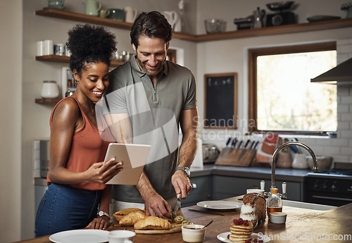 Image of Young couple cooking healthy food together following recipes online on a tablet, step by step. Happy, cheerful and smiling husband and wife making dinner in the kitchen at home.