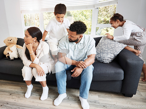 Image of Frustrated, annoyed and irritated couple sitting on the couch with their hyperactive, noisy and naughty kids fooling around on the sofa at home. Man and woman feeling tired while their children play