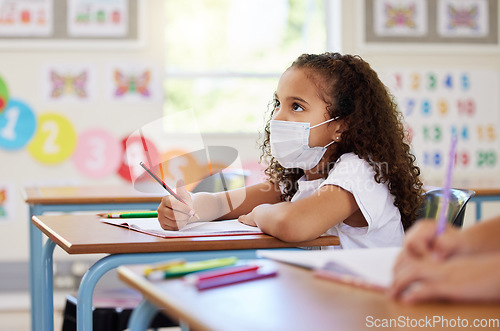 Image of Education, classroom and learning with covid face mask on girl doing school work, writing and reading at her desk in elementary class. Elementary child wearing protection to stop the spread of virus