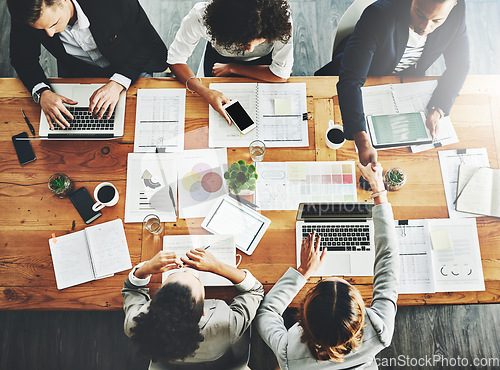 Image of Handshake greeting before a business meeting proposal of collaboration and teamwork. Above view of creative office team and marketing agents working on graphs, data and information