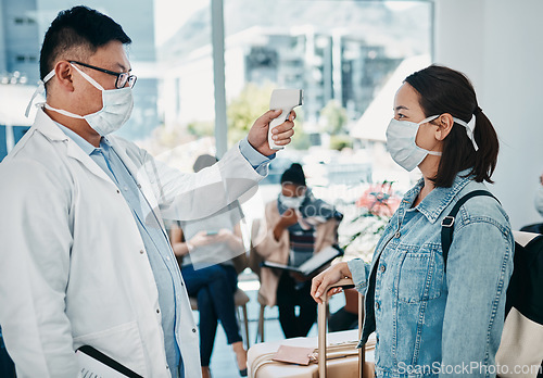 Image of Covid traveling with a doctor taking temperature of a woman wearing a mask in an airport for safety in a pandemic. Healthcare professional with an infrared thermometer following travel protocol