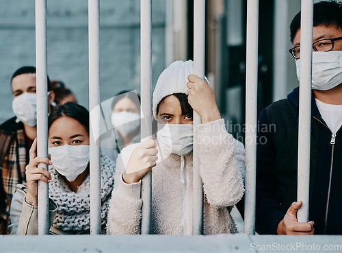 Image of Foreign people in isolation wearing covid face mask at the border or in quarantine or airport looking unhappy, upset and angry. Poor refugees, immigrants and tourists stuck behind a gate in lockdown