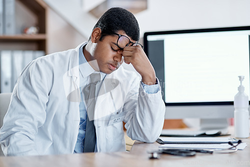 Image of Stressed, tired young male doctor at his office desk in a hospital. Medical or healthcare man exhausted with pain and headache or sore eyes at the workplace from overworking and burnout