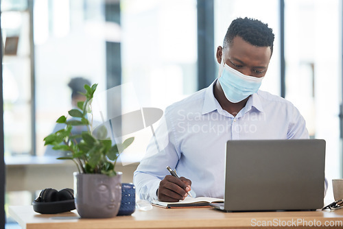 Image of Covid, mask and business man working in quarantine during a pandemic at the office or workplace for safety. Man alone taking or writing important notes while at work on a laptop and being productive.