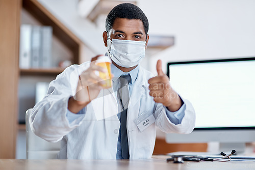 Image of Trustworthy doctor selling good covid medicine or bottle of pills, approving successful medication in hospital. Male healthcare or medical professional wearing mask, showing thumbs up hand gesture.