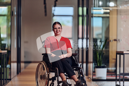 Image of A modern young businesswoman in a wheelchair is surrounded by an inclusive workspace with glass-walled offices, embodying determination and innovation in the business world