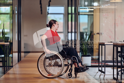 Image of A modern young businesswoman in a wheelchair is surrounded by an inclusive workspace with glass-walled offices, embodying determination and innovation in the business world