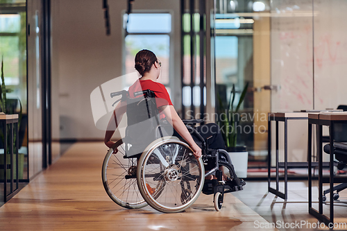 Image of A modern young businesswoman in a wheelchair is surrounded by an inclusive workspace with glass-walled offices, embodying determination and innovation in the business world