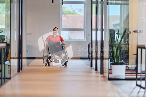 Image of A modern young businesswoman in a wheelchair is surrounded by an inclusive workspace with glass-walled offices, embodying determination and innovation in the business world