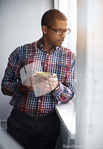 Image of Business man taking a break while looking out of the window. African American male relaxing indoors by viewing outside urban activity. Office worker watching city life below the building.