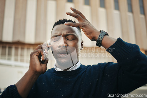 Image of Tired, angry and stress business man talking on an annoying phone call outdoors in a city. Frustrated, pain or sick black male entrepreneur with a headache or migraine outside a urban town